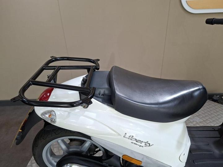 A close-up of a white scooter with a black seat and a rear luggage rack, set against a neutral background.