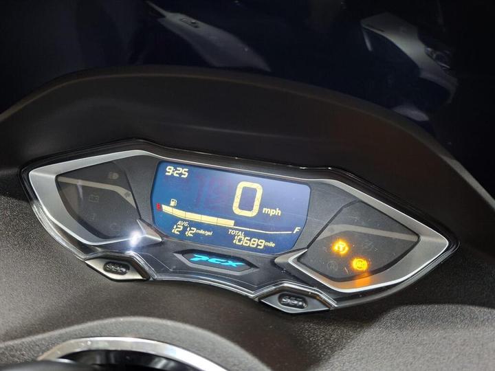 Close-up of a motorcycle dashboard display showing the time as 9:25, speed at 0 mph, average mileage of 12 miles per gallon, and total distance of 1069 miles, with warning indicators illuminated.