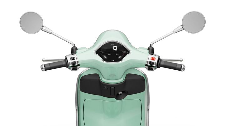 Close-up view of a scooter's handlebar, featuring a mint green dashboard with a digital display, two mirrors, and control levers on either side.