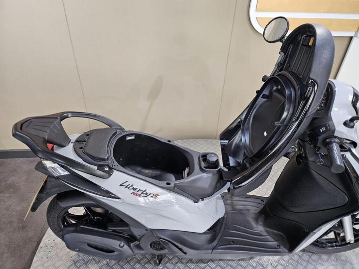 A gray scooter with the brand name "Liberty S" displayed, featuring an open storage compartment under the seat and a sleek, modern design.