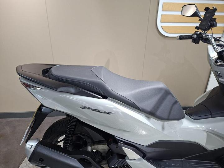 A close-up view of a motorcycle seat, showcasing a sleek, modern design in gray and white, with visible suspension components and a minimalist background.