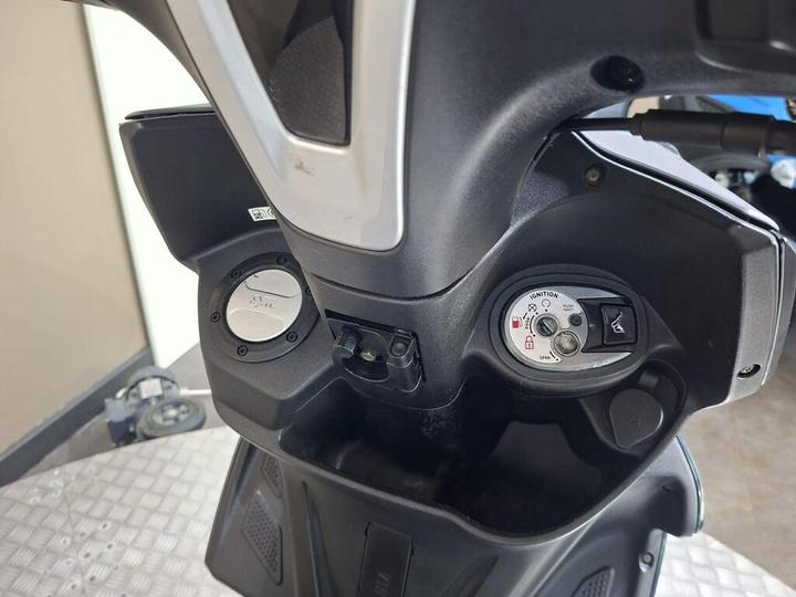 Close-up view of a scooter's dashboard, featuring the ignition switch, fuel gauge, and various controls, set against a textured surface.