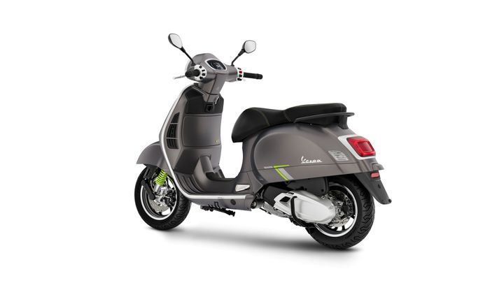 A stylish gray Vespa scooter viewed from a slight rear angle, showcasing its sleek design, vibrant green shocks, and modern features.