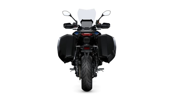 A rear view of a motorcycle with a prominent tire and black side panniers, featuring a clear windscreen, handlebars with mirrors, and a small display panel.