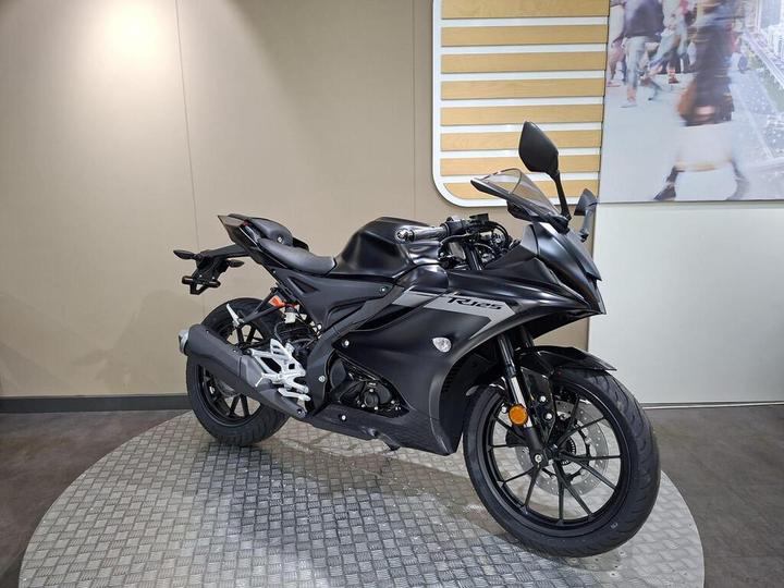 A sleek black motorcycle with a sporty design, displayed on a textured surface in a modern showroom setting.