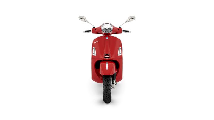 A front view of a red scooter with a classic design, featuring a round headlight and chrome mirrors.