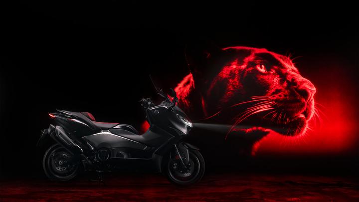 A sleek black motorcycle is illuminated against a dark background, featuring a vivid red projection of a panther's face, showcasing its intense gaze and whiskers.
