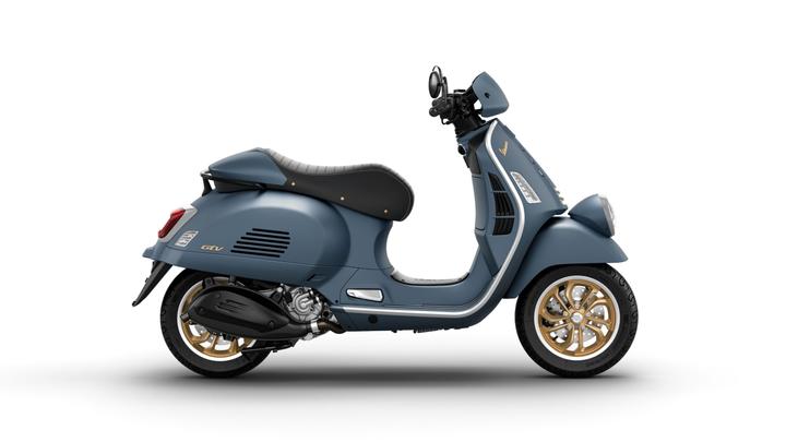 A stylish blue Vespa scooter with gold rims and a black seat, viewed from the side.