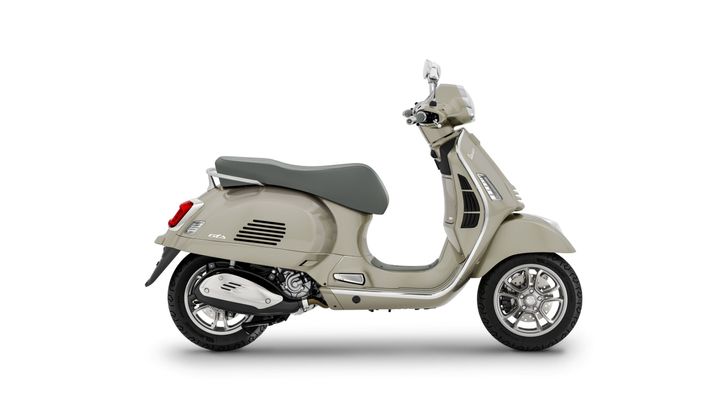 A side view of a light beige Vespa scooter with a grey seat and chrome details, showcasing its classic design and modern features.