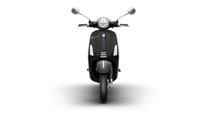 Front view of a black Vespa scooter against a white background, showcasing its classic design, round headlight, and chrome mirrors.