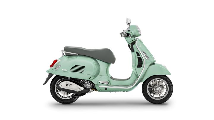 A mint green Vespa scooter viewed from the side, featuring a sleek design, cushioned seat, and chrome details.