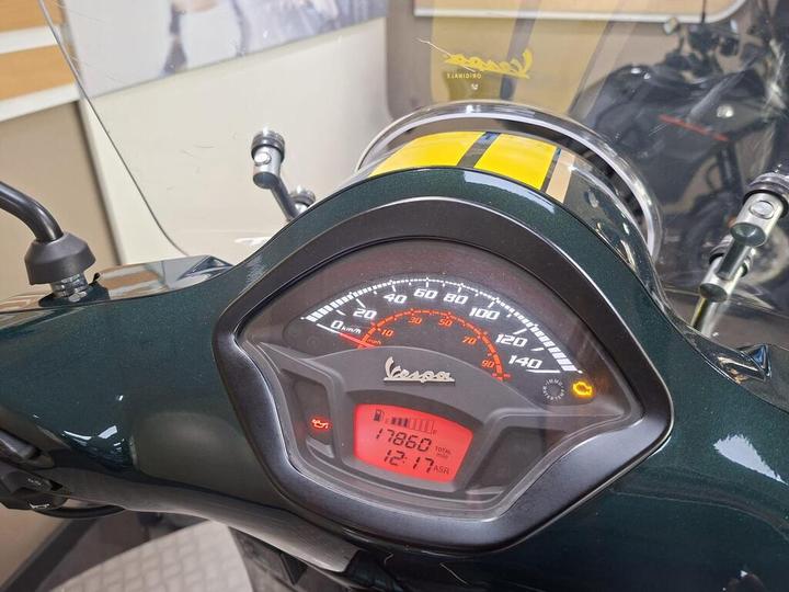 A close-up view of a motorcycle dashboard showing a speedometer and odometer with a reading of 17860 km, and various indicator lights, set against a blurred background.