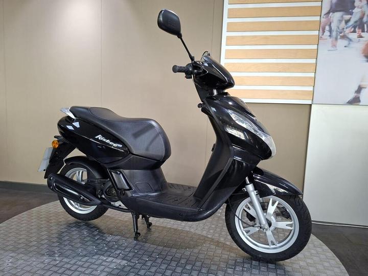 A black scooter is displayed on a textured floor against a neutral background, showcasing its design and features.