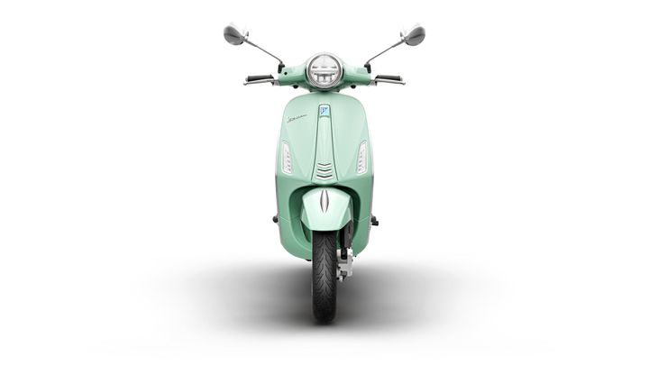 A front view of a mint green scooter against a white background, showcasing its sleek design, circular headlight, and handlebars with mirrors.