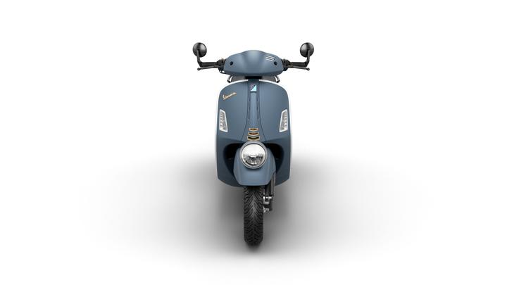 A front view of a blue vintage-style scooter with a rounded design, showcasing the handlebars, headlight, and distinctive branding.