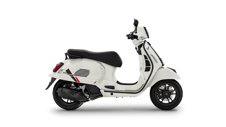 A white scooter with a sleek design, featuring black accents and a comfortable black seat, positioned side-on against a plain background.