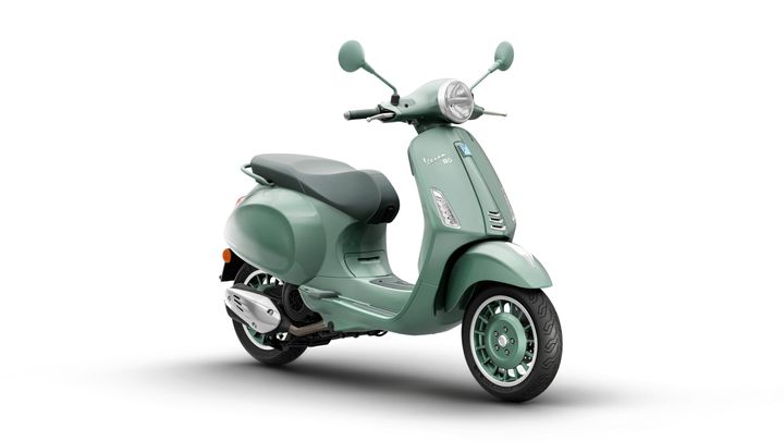 Vespa Primavera 80th 125 A mint green scooter with a sleek design, featuring a comfortable seat and stylish wheels, positioned at an angle against a white background.