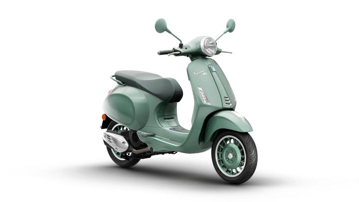 Vespa Primavera 80th 125 A mint green scooter with a sleek design, featuring a comfortable seat and stylish wheels, positioned at an angle against a white background.