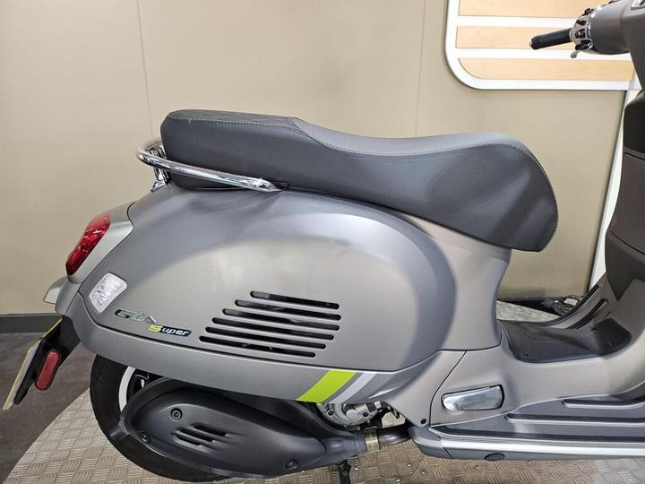 A close-up view of the rear side of a gray scooter, featuring a sleek seat, chrome accents, and a vibrant green stripe on the body.