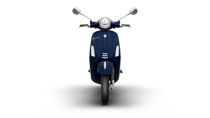 A navy blue scooter is displayed from the front, featuring a round headlight, chrome mirrors, and a sleek design. The background is white, emphasizing the scooter's details.