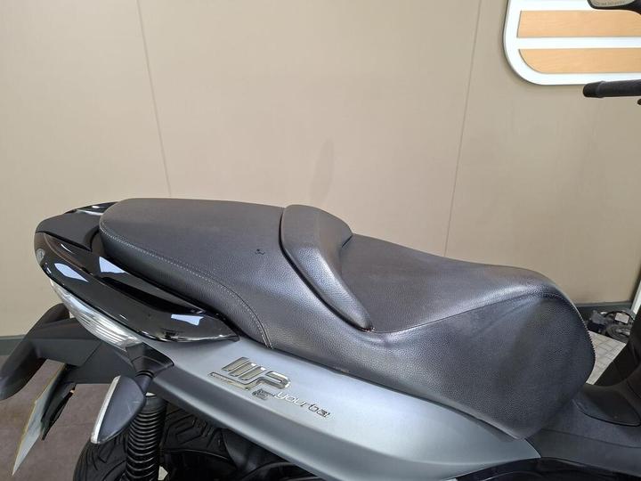 Close-up view of a black leather motorcycle seat with a sleek design, highlighting its smooth surface and contours. The background is neutral, emphasizing the seat's details.