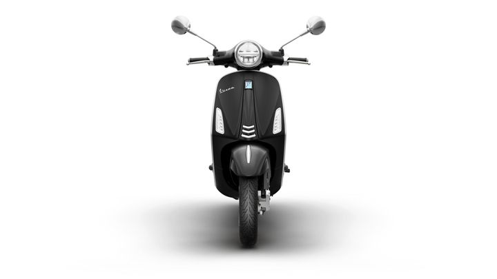 Front view of a black Vespa scooter, showcasing its sleek design, round headlight, and chrome mirrors against a white background.