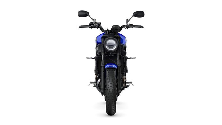 A front view of a blue motorcycle with a round headlight, black handlebars, and a wide tire on a white background.