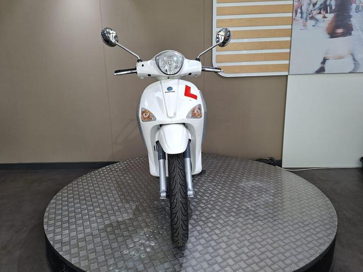 A white scooter with a learner's permit sticker, displayed on a rotating platform against a neutral background. The scooter features a round headlight and chrome mirrors.