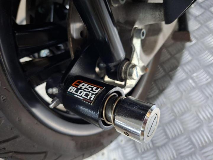 Close-up view of a motorcycle's rear suspension featuring an "Easy Block" component, with a shiny metallic end piece and black housing, mounted on a textured surface.