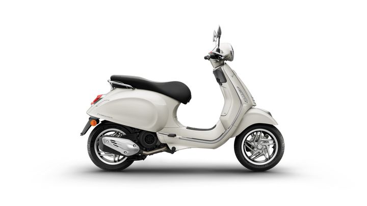 A cream-colored scooter with a black seat, viewed from the side, featuring a chrome exhaust and stylish alloy wheels against a white background.