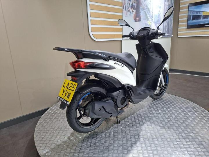A white and black scooter viewed from the rear, displaying the license plate LA25 YVW, set against a plain background with a textured floor.