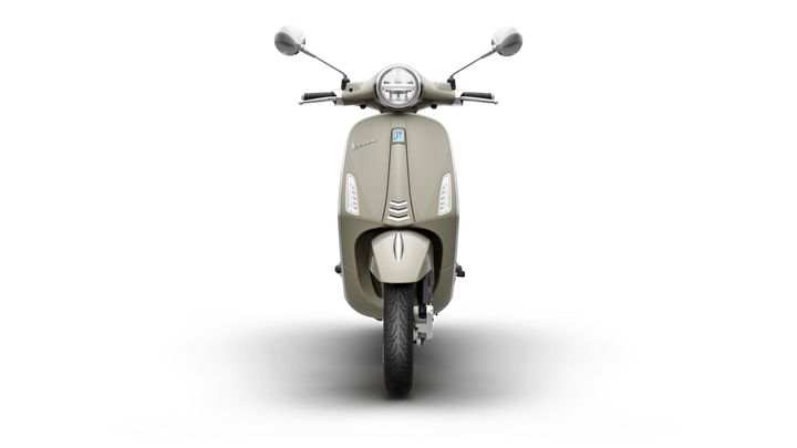A frontal view of a beige scooter with a rounded headlight and sleek body design, mounted on a single tire. The background is plain white, highlighting the scooter's features.