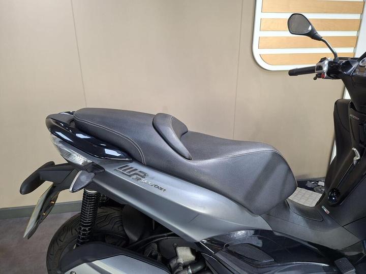 A close-up view of a black scooter seat with a sleek design, set against a neutral background.