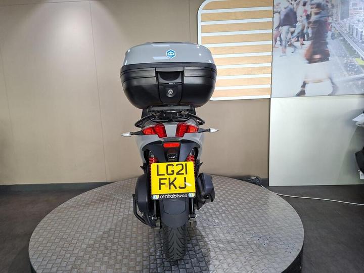 A rear view of a motorcycle with a black top case, featuring a registration plate labeled LG21 FKJ, displayed on a circular platform in a showroom environment.