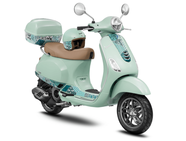 A mint green Vespa scooter with a matching helmet and a storage compartment on the back, featuring patterned detailing on select body parts.