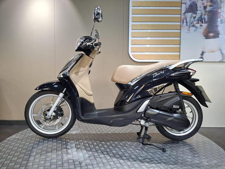A black and cream scooter with a stylish design, displayed on a textured floor, against a neutral background.