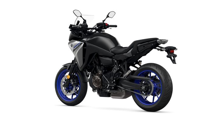A sleek black motorcycle with blue rims, viewed from the rear-left angle, showcasing its modern design, dual-sport tires, and handlebar controls.