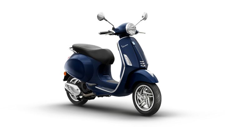 A navy blue Vespa scooter with a sleek design, featuring a black seat, chrome mirrors, and a stylish front light, positioned at a slight angle.