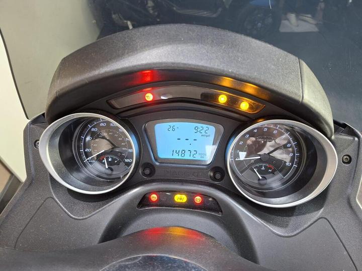 Dashboard display of a scooter showing speedometer, fuel gauge, and trip details, with indicator lights illuminated.