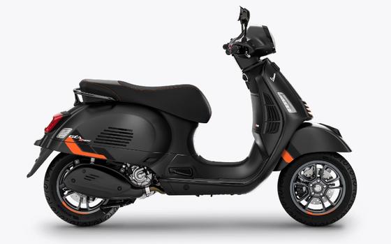 A modern black motor scooter with orange accents and alloy wheels, displayed in a profile view against a clean white background.