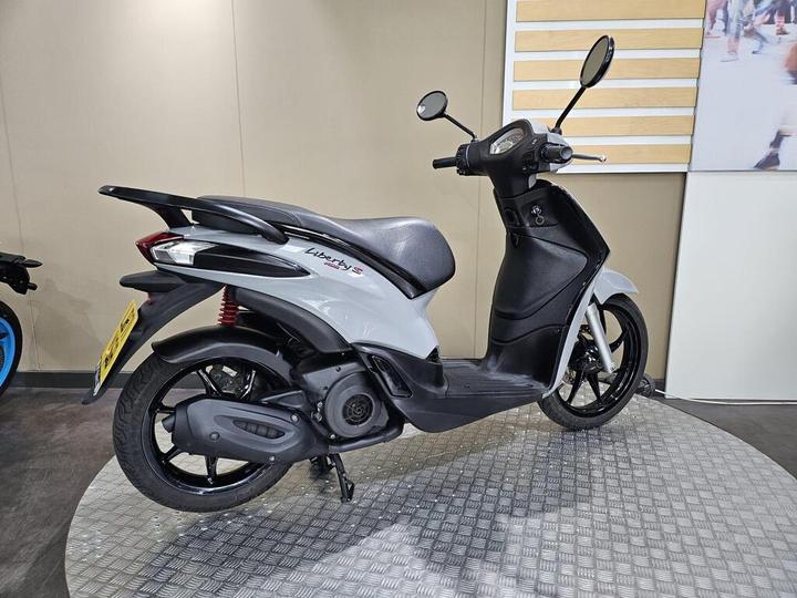 A gray scooter displayed on a circular platform in a showroom, showcasing its sleek design and modern features.