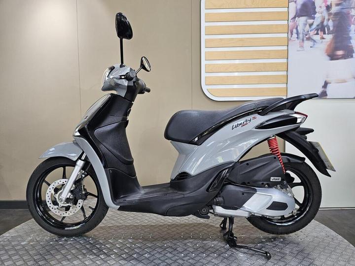 A sleek gray scooter with a black seat, positioned on a textured surface, showcased against a neutral background.