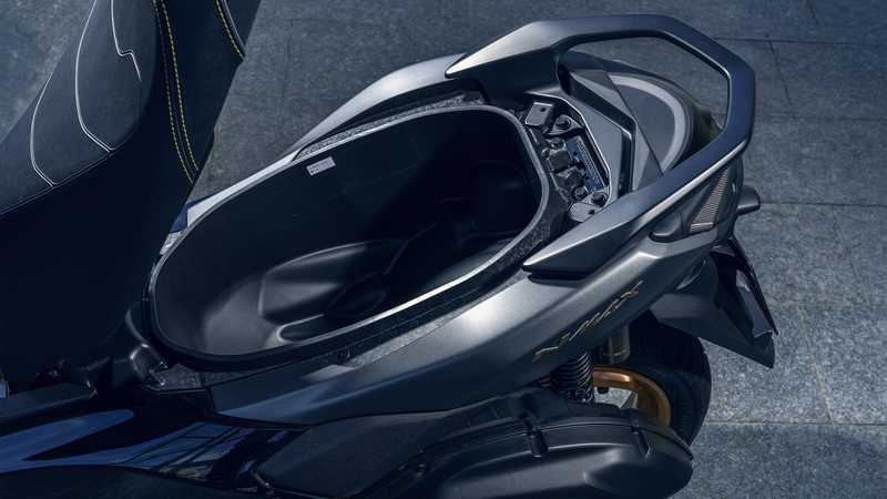 Close-up view of a motorcycle's storage compartment, highlighting the sleek design and textured materials, with the seat and controls partially visible.