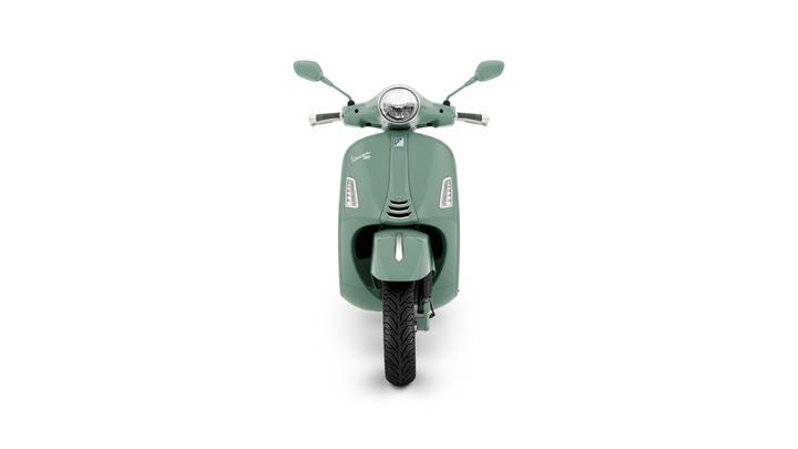 A mint green scooter is shown from the front, featuring a round headlight, sleek body, and a textured tire. The background is plain white, emphasizing the scooter's design.