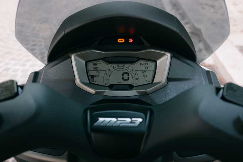 Close-up of a scooter's dashboard displaying a digital speedometer, odometer, fuel level, and various warning lights, with the brand "MP3" visible on the handlebar.