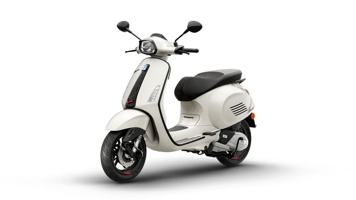 A sleek white scooter with a black seat and red accents, viewed at an angle that highlights its front and side. The scooter features modern design elements, including a windshield, round headlight, and unique body contours.