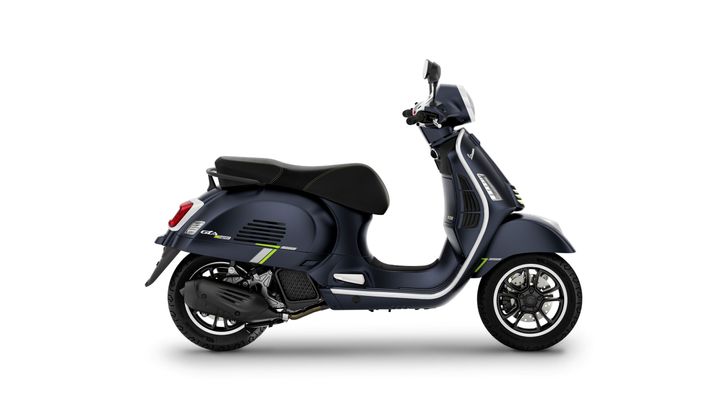 A dark blue Vespa scooter with a sleek design, featuring green accents, seen from the side.