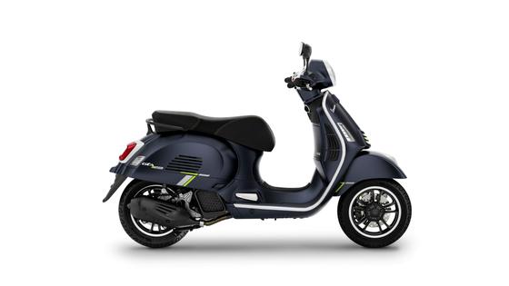 A dark blue Vespa scooter with a sleek design, featuring green accents, seen from the side.