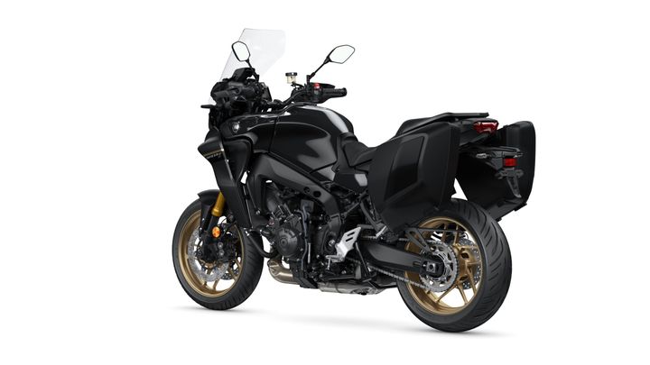A sleek black motorcycle with gold wheels, side panniers, and a tall windscreen, angled to highlight its design and features.