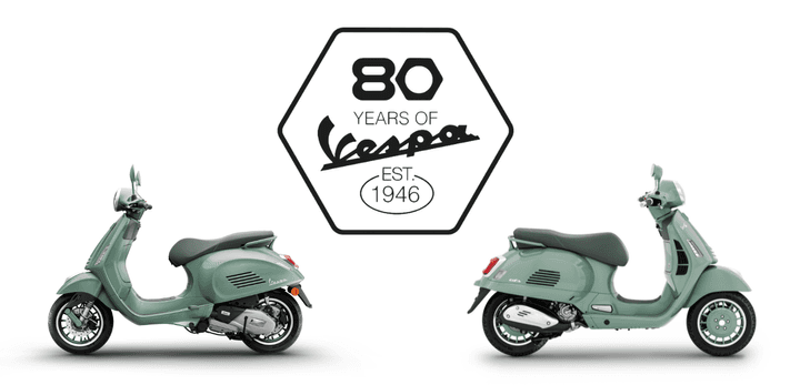 A pair of mint green Vespa scooters positioned side by side, with an emblem celebrating "80 Years of Vespa" established in 1946 displayed between them.